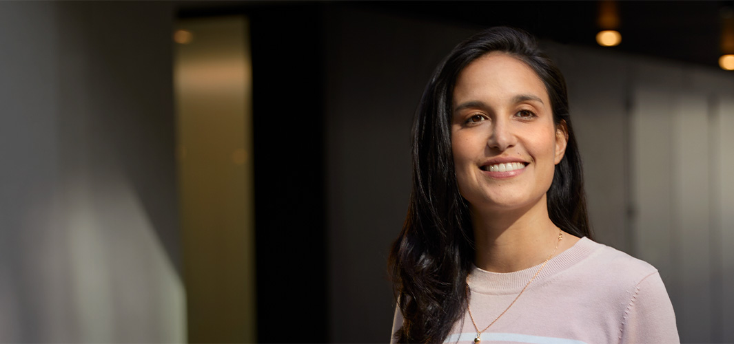 Camila står smilende innendørs i et kontorlandskap.