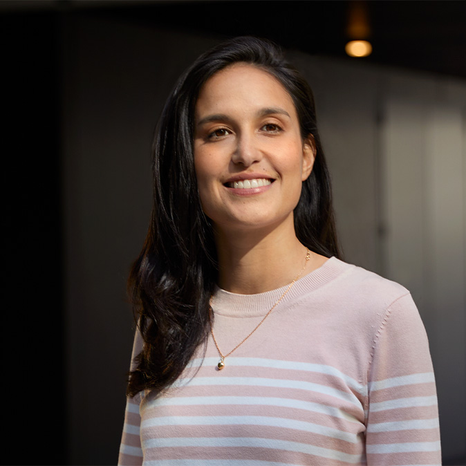 Camila står smilende innendørs i et kontorlandskap.