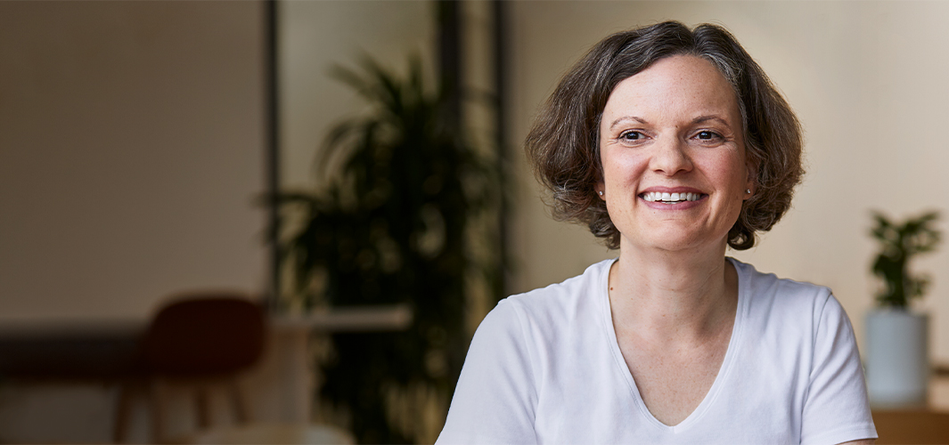 Ruth sitter utendørs og smiler med planter i bakgrunnen.