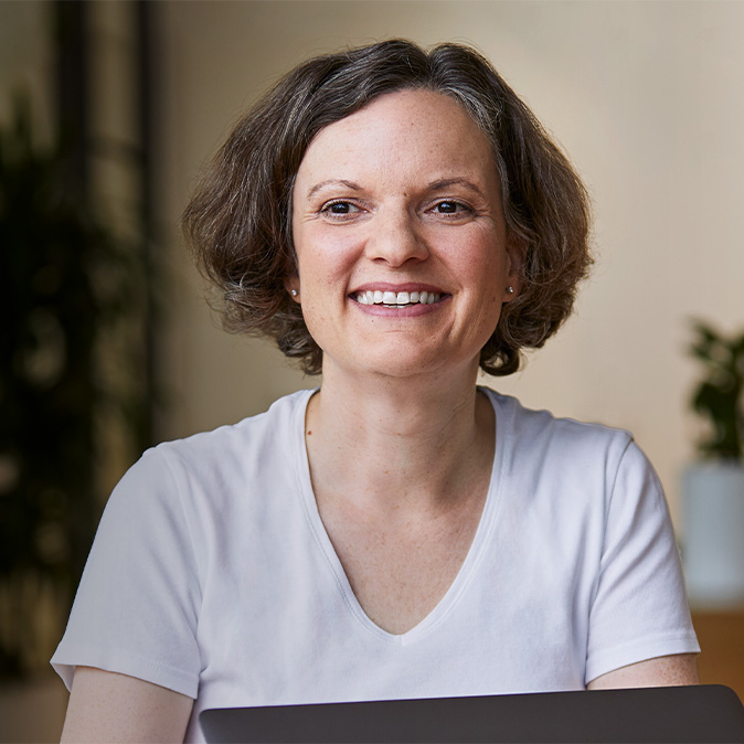 Ruth sitter utendørs og smiler med planter i bakgrunnen.