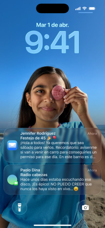 Cinco modelos de iPhone se separan uno detrás del otro, cada modelo se superpone levemente sobre el siguiente, la pantalla del modelo ubicado más a la izquierda muestra una conversación con un fondo en Mensajes, el siguiente muestra la pantalla de inicio con íconos de apps coloridos, el del centro muestra la pantalla bloqueada con una foto y los números de la hora diseñados con Liquid Glass, así como dos notificaciones en la parte inferior de la pantalla, el siguiente modelo hacia la derecha muestra íconos de apps translúcidos en Liquid Glass y el último a la derecha muestra el reproductor de música hecho con Liquid Glass
