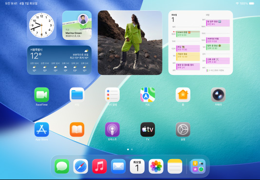 가로 방향으로 놓인 iPad 3대. 가운데 모델이 전면에 배치되고, 상단에는 Apple Pencil 부착. 가운데 화면은 잠금 화면에서 Liquid Glass 효과가 적용된 다채로운 앱 아이콘의 홈 화면으로 전환된 상태. 왼쪽은 미리보기 앱 화면, 오른쪽은 Dock에서 여러 파일이 펼쳐진 홈 화면.