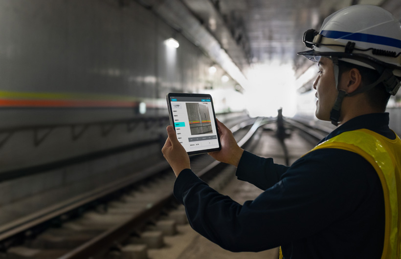 Một nhân viên bảo trì trong đường hầm của Tokyo Metro giơ iPad lên để chụp ảnh đường ray, trong khi đồng nghiệp đang quan sát.