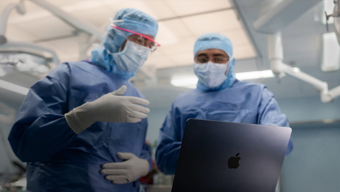 Hai bác sĩ phẫu thuật đang thảo luận về một nội dung trên màn hình của MacBook Pro trong phòng phẫu thuật.